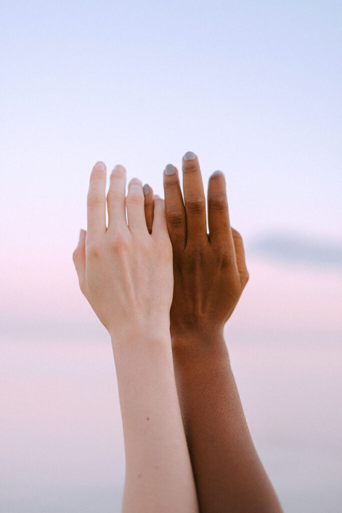 two hands of different skin colour reaching for the sky